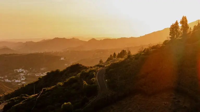 winding road through mountains at sunset with village in distance